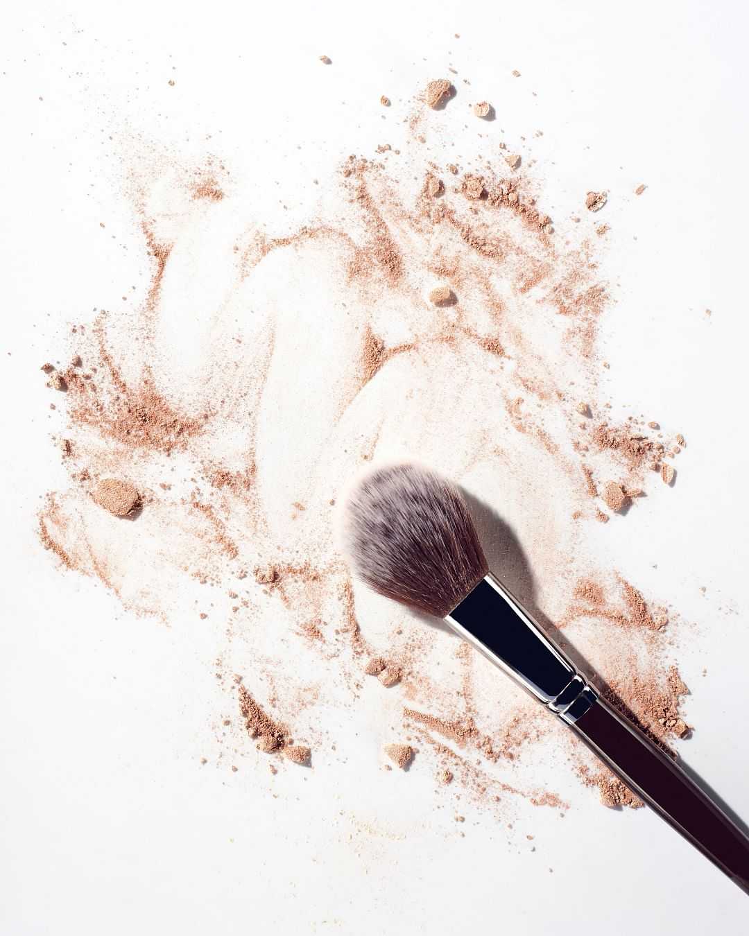 Makeup brush with scattered beige powder on a white surface.