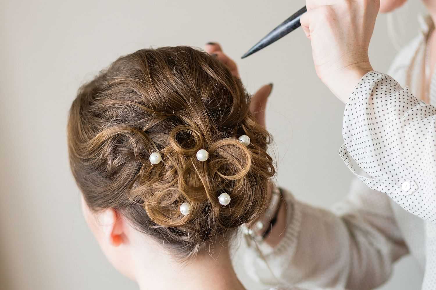 Woman having her hair styled into an elegant updo with pearls by a hairstylist.