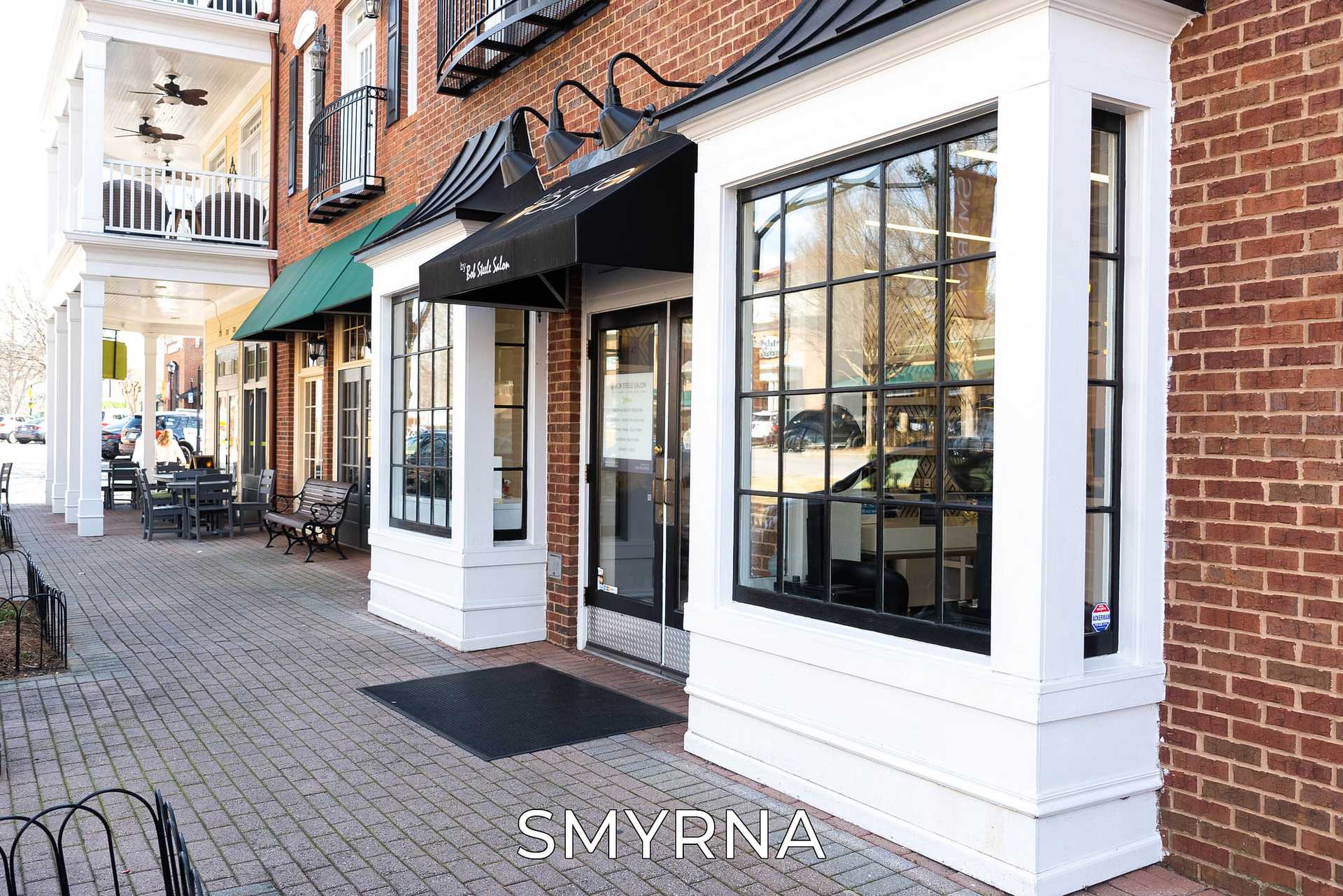 Street view of a brick building with shops, large windows, and outdoor seating. Text: "SMYRNA".