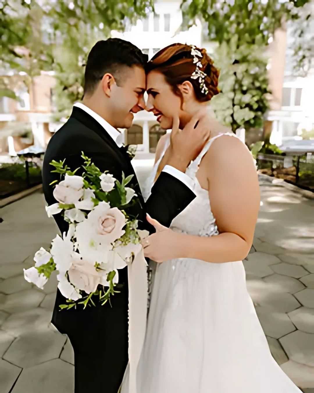 Bride and groom smiling, holding a bouquet, sharing a tender moment outdoors on their wedding day.